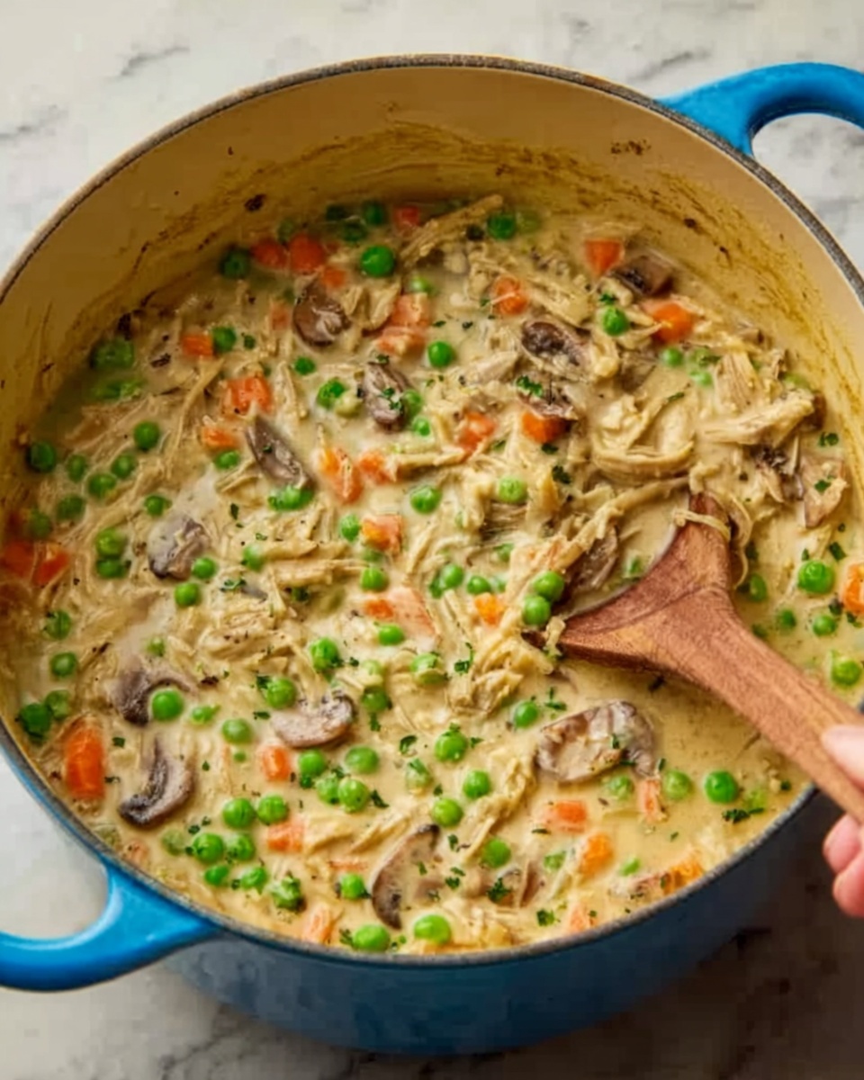 A close-up view of a blue pot filled with a creamy mixture containing shredded pieces of meat, bright green peas, thinly sliced orange carrot pieces, and sliced mushrooms. The creamy sauce appears rich and thick, coating all the ingredients evenly with a soft, smooth texture. A woman's hand is holding a wooden spoon, partially submerged in the mixture, stirring it gently. The pot is sitting on a white marbled surface. photo taken with an iphone --ar 4:5 --v 7