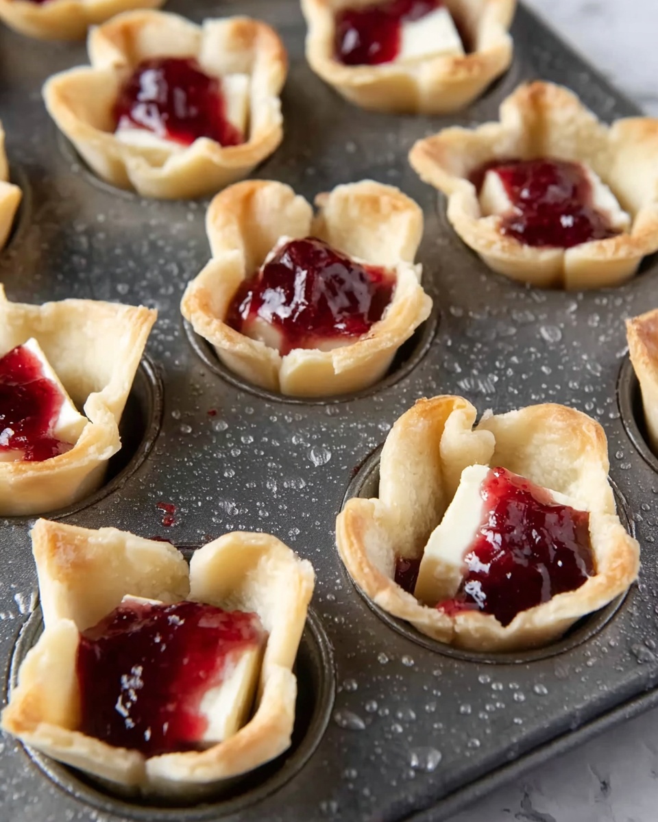 A metal baking tray holds several small tart shells made from light beige dough, each shell forming a cup shape with crimped edges. Inside every tart shell, there is a thick white square of cheese topped with a shiny, deep red jam that looks slightly chunky and sticky, creating a colorful contrast. The tray has small droplets of water scattered on its surface, adding texture. The background is a white marbled surface. photo taken with an iphone --ar 4:5 --v 7