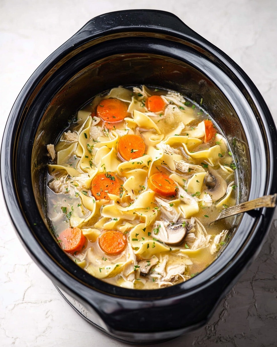 The image shows a black slow cooker filled with chicken noodle soup on a white marbled surface. The soup has several layers including wide flat yellow noodles floating on top, bright orange carrot slices scattered throughout, small pieces of light shredded chicken, and thin white mushroom slices, all submerged in a clear broth with tiny green herb bits sprinkled around. A silver ladle is partially visible on the right side inside the cooker. The black slow cooker contrasts with the bright colors of the soup inside. Photo taken with an iphone --ar 4:5 --v 7