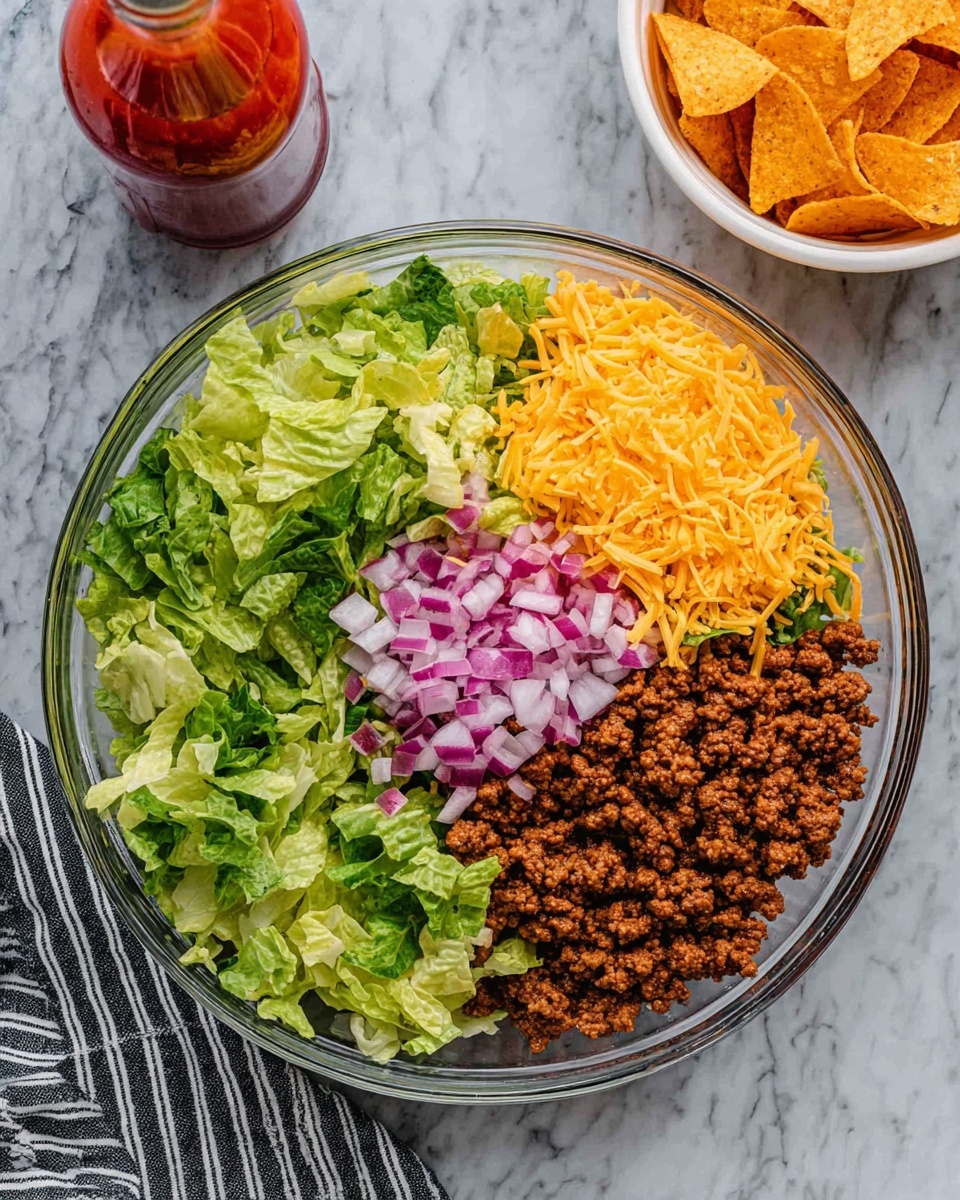 The image shows a clear glass bowl with four layers arranged side by side inside. Starting from the left, there is a fresh green leafy lettuce layer with light and dark shades, next to it is a bright yellow shredded cheese layer with a soft texture, followed by finely chopped purple-red onions with white parts showing, and on the far right, a layer of brown cooked ground beef with a crumbly texture. The bowl is placed on a white marbled surface. In the top right corner, there is a white bowl filled with orange triangular chips, and a bottle of red sauce is positioned next to it. A striped cloth rests on the bottom left edge of the image. Photo taken with an iphone --ar 4:5 --v 7