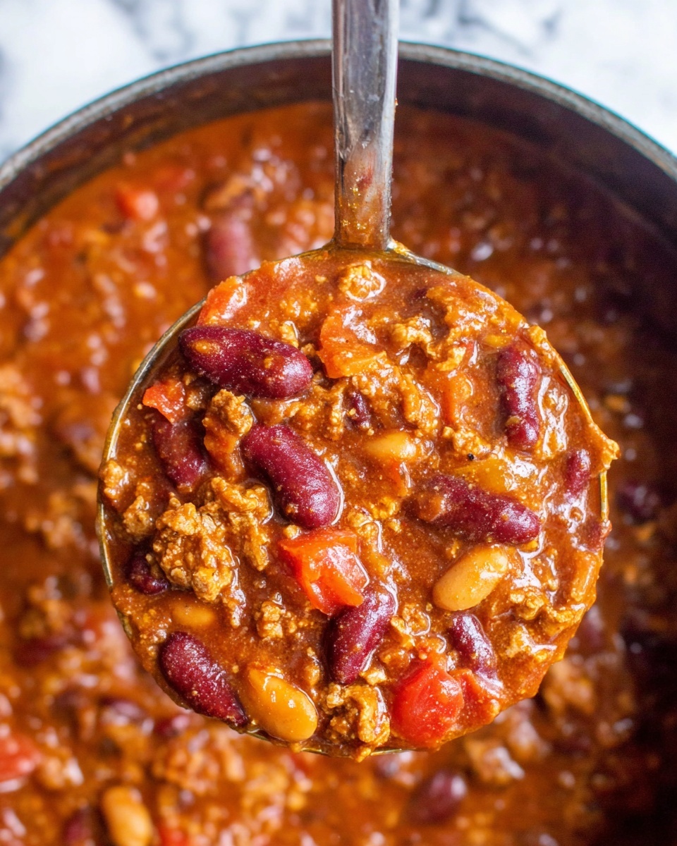 A close-up view of a metal ladle filled with thick, chunky chili featuring layers of deep red kidney beans, light brown beans, and tomato chunks in a rich, reddish-orange sauce with bits of textured ground meat throughout. The background shows the pot full of the same chili with visible beans, tomato pieces, and sauce, all set against a white marbled texture. The glossy sauce envelops the beans and meat pieces, giving a hearty and comforting look. Photo taken with an iphone --ar 4:5 --v 7