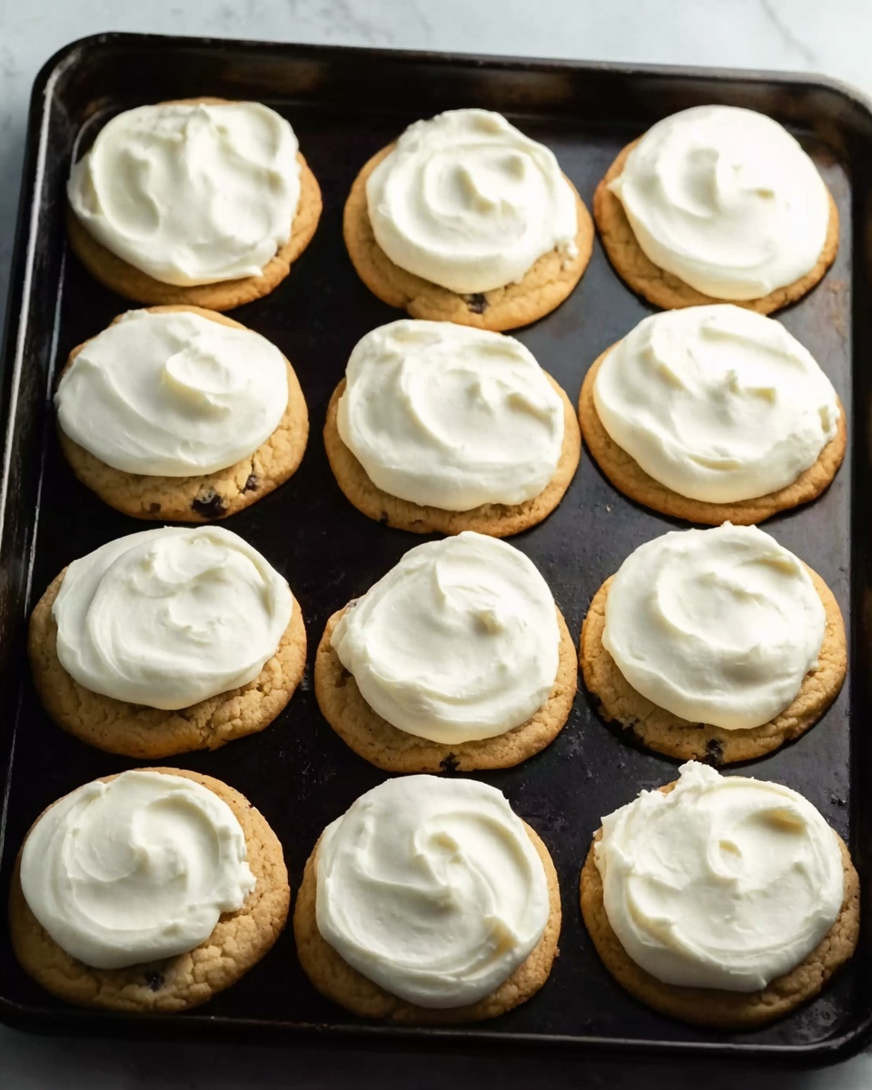 A black baking tray filled with ten round cookies evenly spaced apart. Each cookie has a light golden-brown base with a slightly crumbly texture and is topped with a thick layer of smooth white frosting spread evenly but with small waves and swirls. The background is a white marbled surface that contrasts with the dark tray. photo taken with an iphone --ar 4:5 --v 7