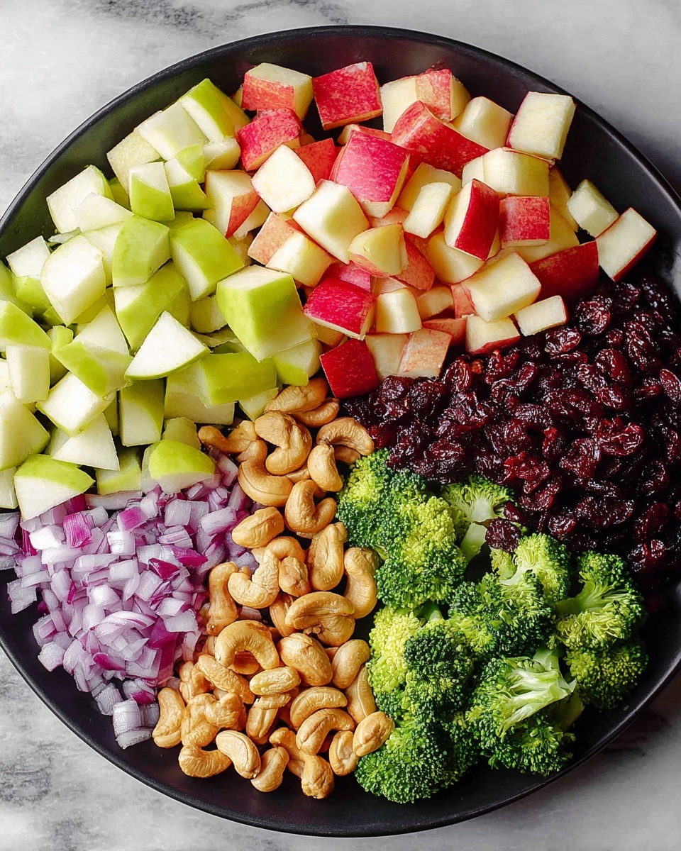 A round black plate holds six separate piles of ingredients arranged in a circular pattern on a white marbled surface. Starting from the top left and moving clockwise, there are small cubes of red apple with red skin and white flesh, followed by similarly sized cubes of green pear with light green skin and white flesh. Next, there is a pile of dark red dried cranberries, then a cluster of whole light brown cashew nuts. Near the bottom left, there are finely chopped pieces of purple-red onion, and finally bright green broccoli florets. Each ingredient is clearly separated from the others, showing their different textures and colors. Photo taken with an iphone --ar 4:5 --v 7