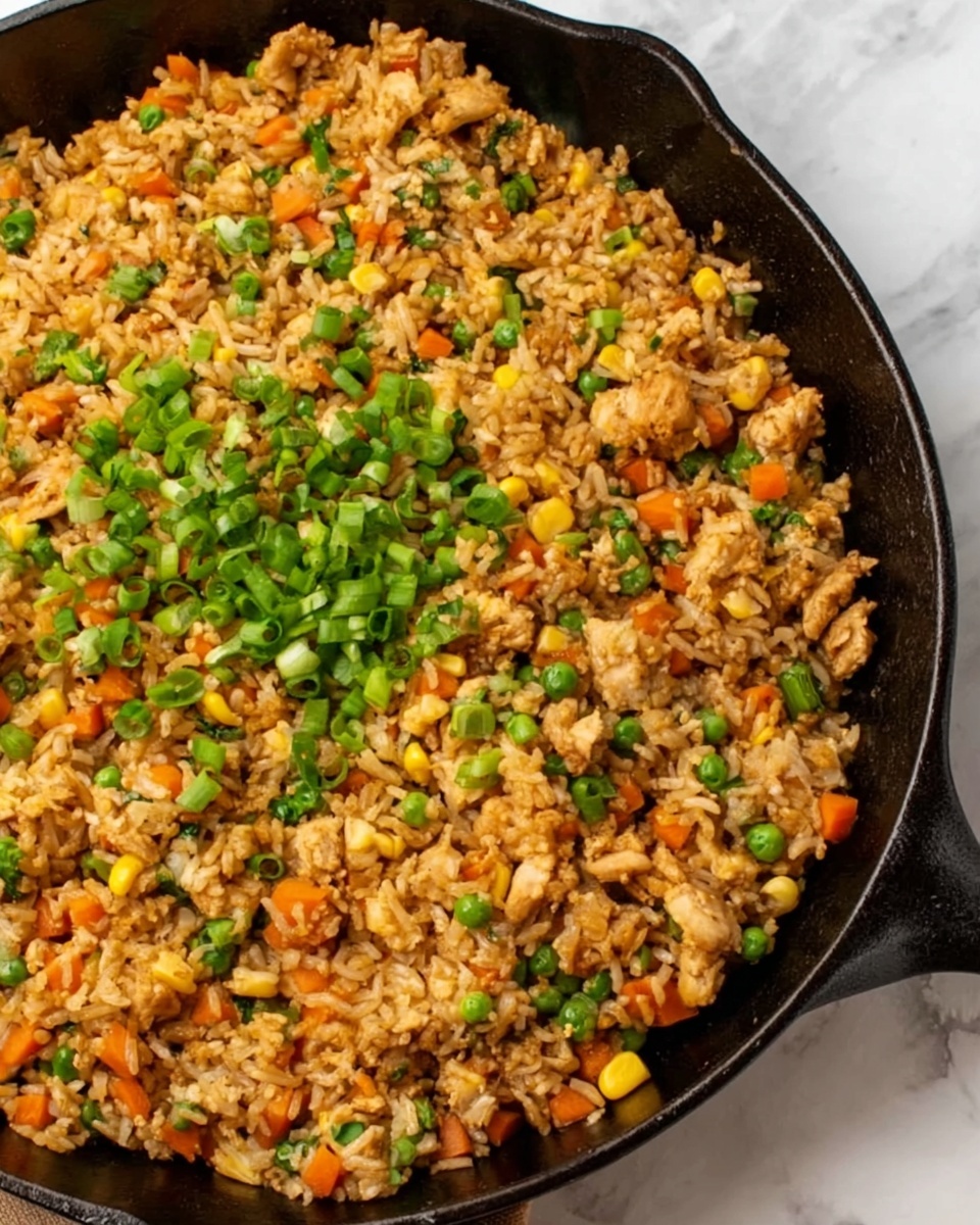 A round white bowl filled with fried rice that has several layers of colors and textures visibly mixed together. The base is light brown rice with a shiny, soft texture. Mixed into the rice are bright orange small carrot cubes, green peas, and small pieces of cooked chicken in a tan color. There are also bits of scrambled egg in yellow scattered evenly throughout. On top, small slices of fresh green onions are sprinkled as a garnish. The bowl sits on a wooden table with a white marbled background partially visible. Photo taken with an iphone --ar 4:5 --v 7
