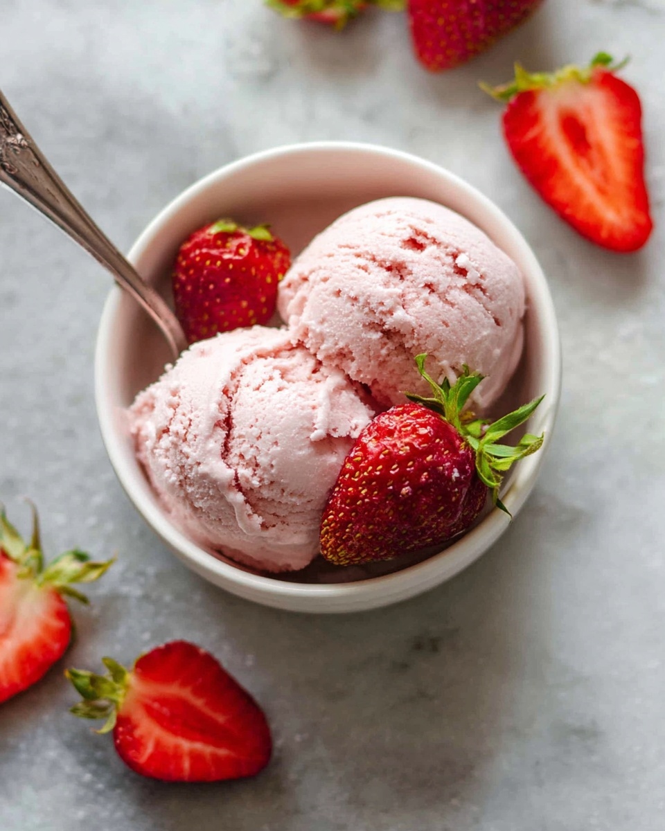 A small white bowl holds two scoops of light pink strawberry ice cream with a slightly creamy and smooth texture. On top, two fresh whole strawberries with bright red skin and green leaves rest, adding vibrant color. A silver spoon is partially inserted into the ice cream. Around the bowl, there are a few whole strawberries and halved strawberries scattered on a white marbled surface. The scene is bright and fresh, showing the ice cream and strawberries as the main focus. photo taken with an iphone --ar 4:5 --v 7
