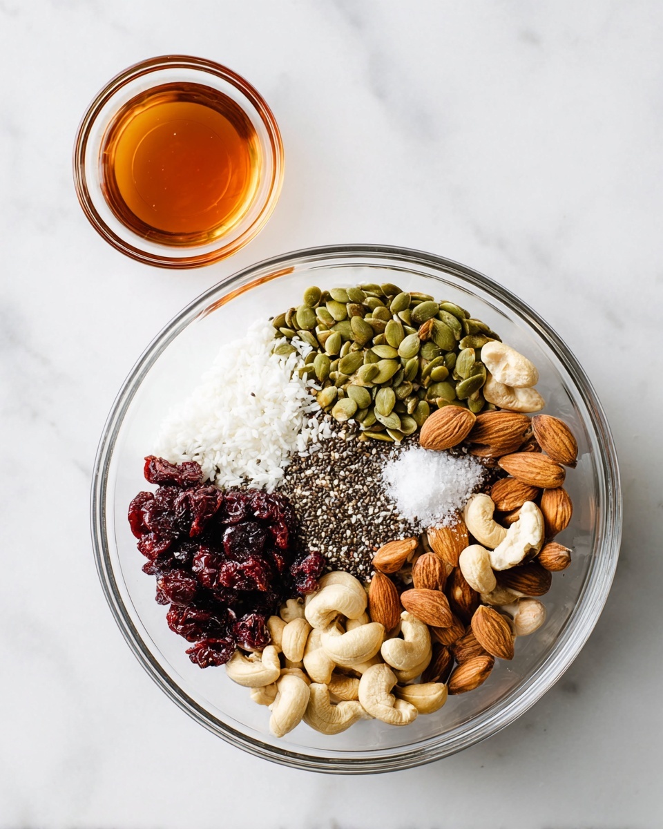 A clear glass bowl sits on a white marbled surface, filled with layers of different dry ingredients arranged side by side. From top right moving clockwise, the first layer is green pumpkin seeds, followed by white coconut flakes, dark red dried cranberries, whole light brown almonds, black chia seeds mixed with a small pile of white coarse salt, and pale cashew nuts. Above the bowl to the top left is a small clear glass bowl filled with amber-colored liquid. The whole scene is bright and clean. photo taken with an iphone --ar 4:5 --v 7