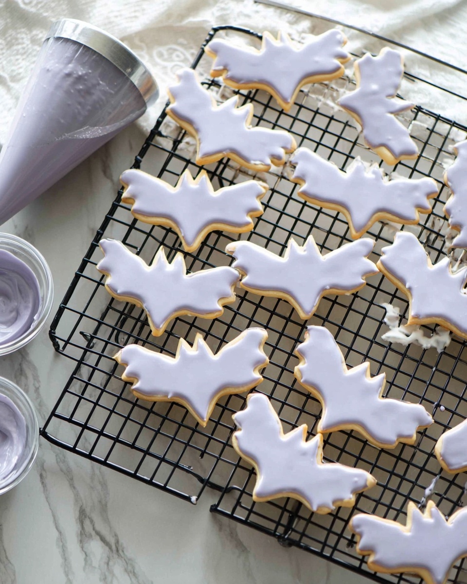 The image shows a black wire cooling rack with several bat-shaped cookies arranged on it. Each cookie has a single layer and is covered entirely with light purple icing that has a smooth texture and some small holes or gaps revealing the cookie beneath. To the left of the rack, there is a piping bag filled with the same purple icing lying on a white marbled surface, along with a small bowl also containing the purple icing. The overall setting has a clean and bright look with the cooling rack and cookies being the main focus. Photo taken with an iphone --ar 4:5 --v 7