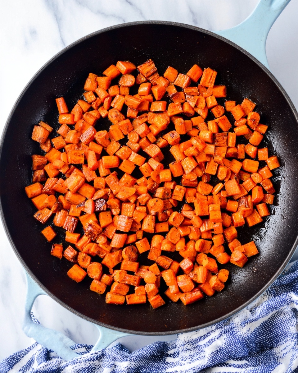 This image shows many small, orange cubes of roasted sweet potatoes spread evenly over a black pan. The sweet potato pieces vary slightly in size but are mostly small and have a soft texture with some edges showing a bit of caramelized browning or slight charring, giving a mix of bright and deeper orange colors. The pan's dark surface contrasts with the vibrant orange cubes, highlighting their roasted texture and slight shine from oil. photo taken with an iphone --ar 4:5 --v 7