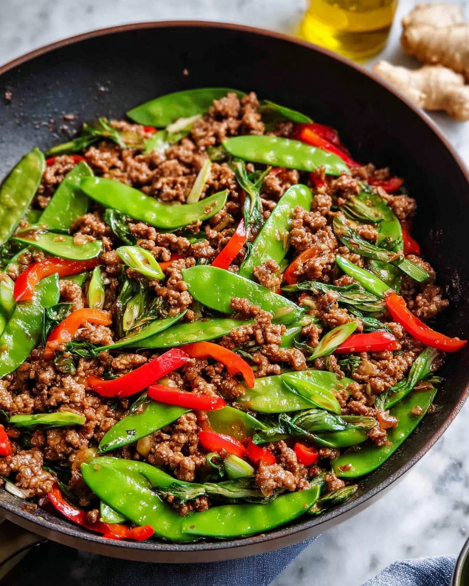 A close-up top view of a black pan filled with cooked ground meat mixed with bright green snow peas, vivid red bell pepper slices, and pieces of green onion, all coated lightly with oil giving a shiny texture; the colors contrast well with the black pan, which rests on a white marbled surface with ginger roots and a jar of oil in the background, photo taken with an iphone --ar 4:5 --v 7