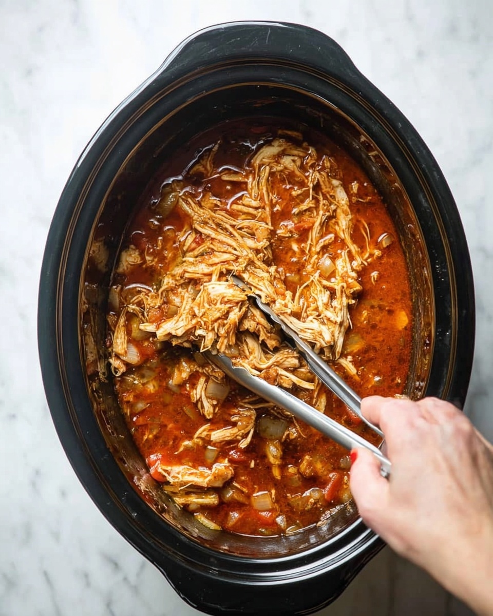 Inside a black slow cooker, there is a mixture of shredded light brown chicken sitting in a thick reddish-brown sauce with visible small pieces of vegetables like onions. A pair of silver metal tongs held by a woman's hand is lifting some of the shredded chicken from the sauce. The slow cooker is placed on a white marbled surface. photo taken with an iphone --ar 4:5 --v 7