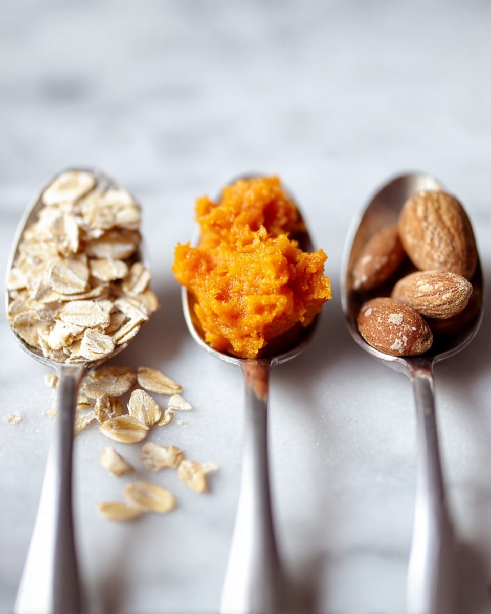 The image shows three metal spoons placed in a row on a white marbled surface. The spoon on the left holds a small pile of light beige rolled oats with a few pieces scattered nearby. The middle spoon is filled with bright orange, soft pumpkin puree, with a rough and thick texture. The spoon on the right contains several whole almonds with a brown shell and a slightly rough surface. The background is softly blurred, highlighting the spoons and their contents. Photo taken with an iphone --ar 4:5 --v 7