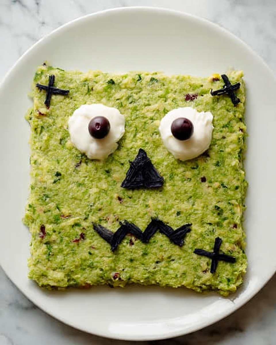 A square serving of green mashed texture shaped like a monster face lies on a white plate on a white marbled surface. The monster face has two dollops of white cream for eyes, each topped with a small dark round piece, a single dark olive nose in the center, and a jagged mouth created with thin dark lines. It has two small round dark shapes on each lower corner resembling ears. Three small dark crosses are placed on the top right corner of the square to give the look of stitches. The mashed green base is speckled with bits of darker green and reddish pieces, giving it a coarse texture. photo taken with an iphone --ar 4:5 --v 7