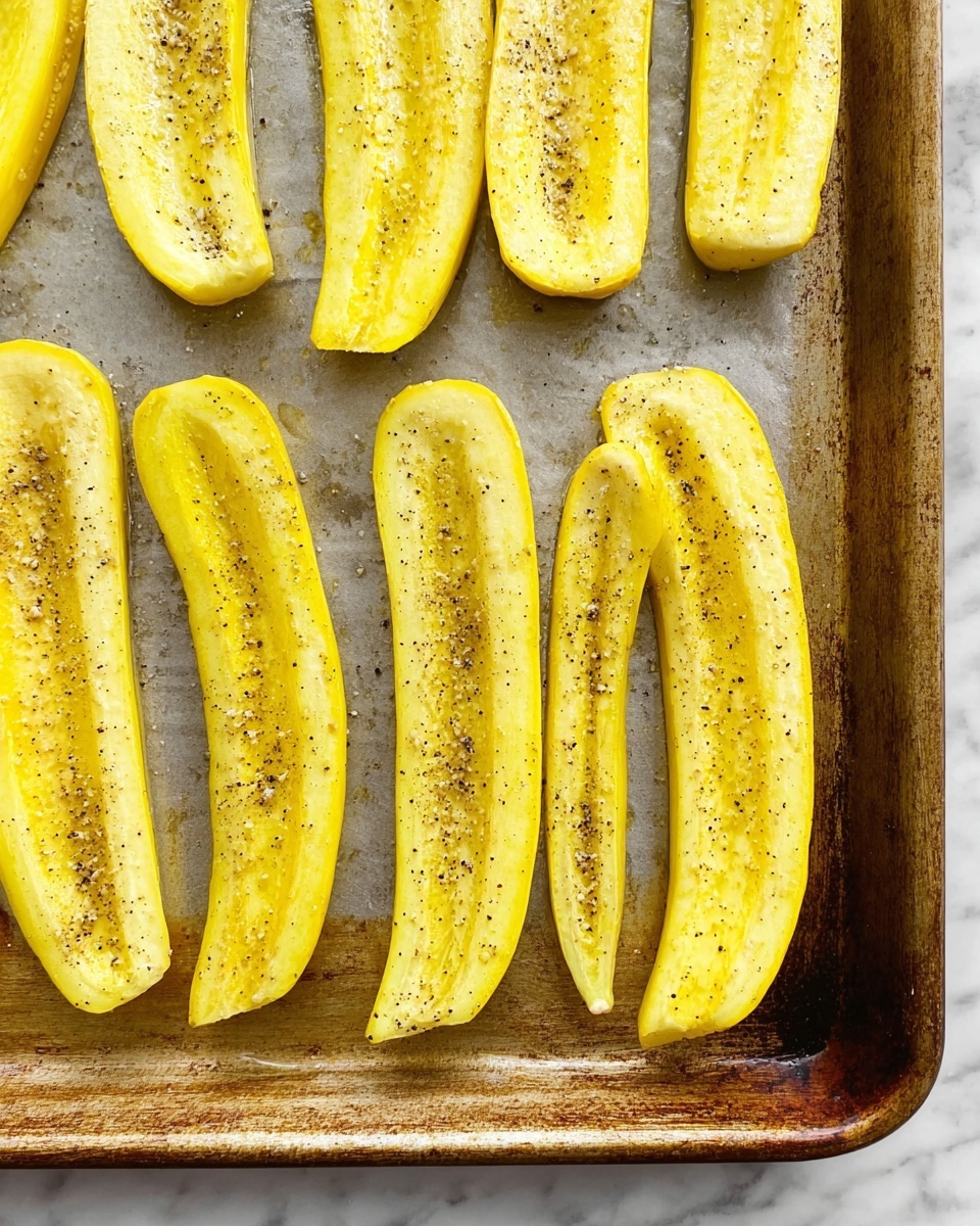 The image shows several long yellow zucchini halves placed in a single layer on a baking sheet. Each zucchini half is yellow on the outside with a pale greenish-white inner flesh that has a soft, slightly textured surface. The flesh is seasoned with small black pepper specks and salt crystals, giving a light speckled appearance. The baking sheet is on a white marbled surface. The zucchinis are arranged neatly with their cut sides facing up, filling most of the baking sheet. The lighting highlights their fresh, cooked look. photo taken with an iphone --ar 4:5 --v 7