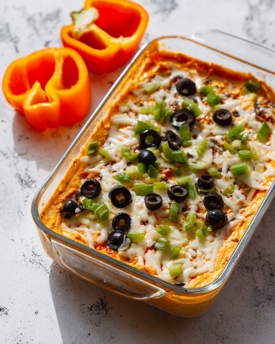 The image shows a clear rectangular glass dish filled with a layered dip. The bottom layer is a smooth, creamy orange spread. Above this is a layer of melted white cheese with visible stringy texture. Scattered on top are chopped green bell peppers and sliced black olives, adding green and dark round spots. The dish sits on a white marbled surface, with two bright orange bell pepper slices placed nearby on the top left. The light in the photo is soft and natural, highlighting the colors clearly. photo taken with an iphone --ar 4:5 --v 7