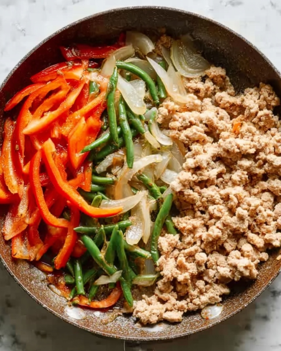 A round pan filled with three clear sections: on the left, long slices of red bell peppers and green beans cooked with a soft, slightly shiny texture; in the middle, light round slices of cooked onion with a translucent look; on the right, a large portion of finely crumbled light beige cooked meat with a tender and dry texture. The pan rests on a white marbled surface. Photo taken with an iphone --ar 4:5 --v 7