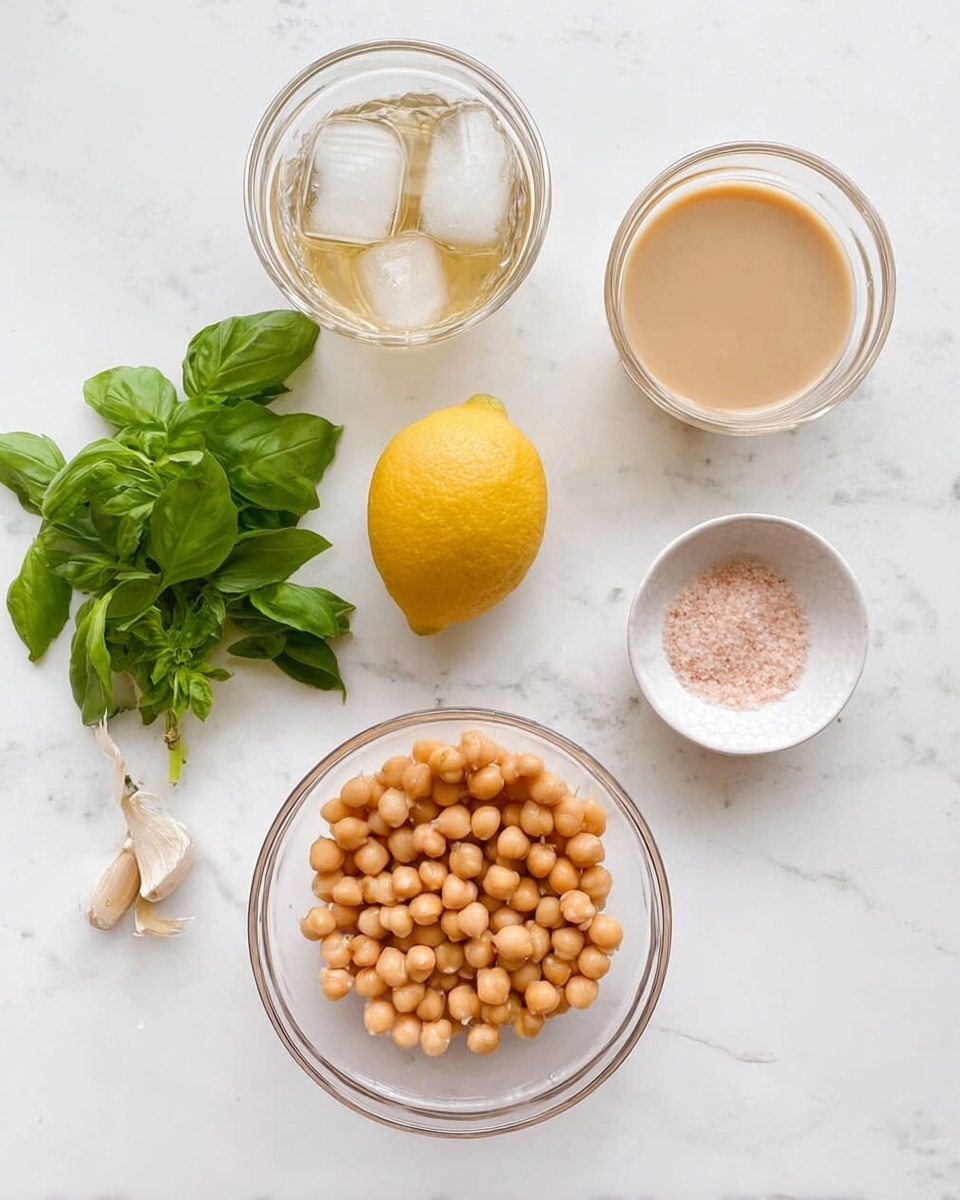 The image shows a white marbled surface with several ingredients arranged neatly. At the center bottom, there is a clear glass bowl filled with round, light brown chickpeas. To the right of this bowl is a whole yellow lemon with a smooth texture. Above the lemon, there is a small white bowl holding pink salt. To the top right, a separate clear glass bowl contains a creamy, light beige liquid. On the top left, another clear glass bowl holds a light brown liquid with two ice cubes floating on top. To the bottom left of all these bowls, there is a bunch of fresh green basil leaves with a sprig of basil flowering on the top. A single garlic clove is placed near the top center of the frame. photo taken with an iphone --ar 4:5 --v 7