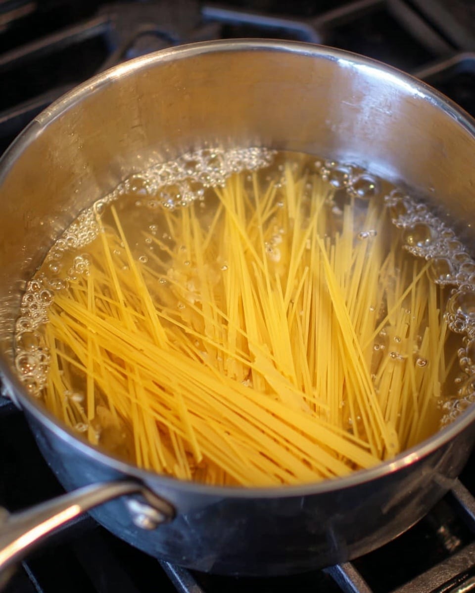 A large silver pot filled with clear water shows uncooked light yellow spaghetti noodles that are partially submerged and spread loosely inside the pot. Small bubbles appear on the water surface, indicating it is just starting to boil. The pot rests on a stove with metal parts visible around it. The scene is simple and focused on the spaghetti inside the pot. photo taken with an iphone --ar 4:5 --v 7