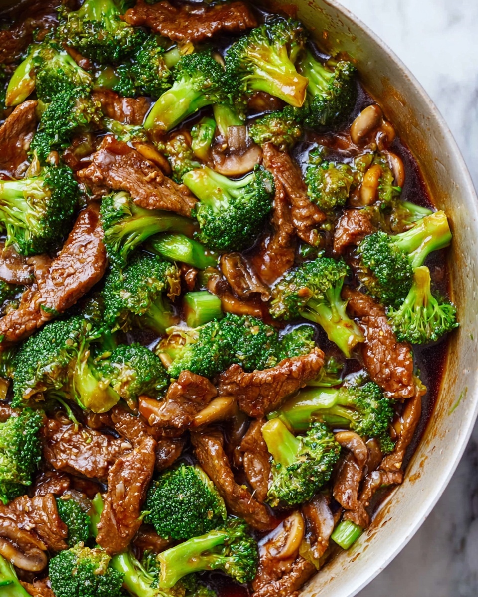 A close-up view of a white pan filled with beef and broccoli stir-fry. The dish has many pieces of bright green broccoli with visible texture and small stalks, mixed with tender slices of brown beef coated in a shiny, rich dark sauce. There are also bits of light brown cooked mushrooms scattered throughout, adding more texture. The sauce glistens and slightly pools at the bottom of the pan, covering the ingredients evenly. The background shows a white marbled surface, enhancing the colors of the food. Photo taken with an iphone --ar 4:5 --v 7