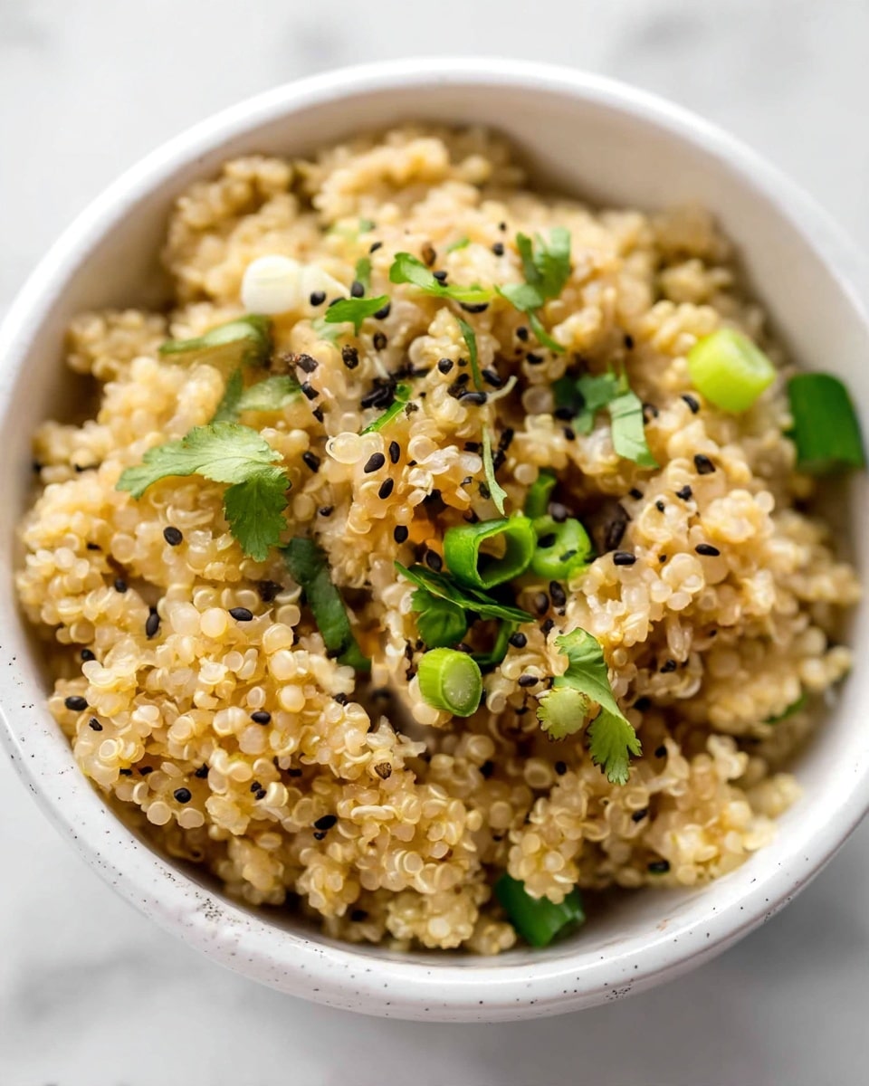 A close-up of a white bowl filled with cooked light tan quinoa, showing small, round grains with a soft texture. The quinoa is topped with small bright green pieces of chopped scallions and fresh cilantro leaves scattered across the surface. Tiny black sesame seeds are sprinkled evenly on top, adding contrast to the beige quinoa and green herbs. The bowl sits on a white marbled surface, and the image captures the fine details of the food's texture and colors. photo taken with an iphone --ar 4:5 --v 7