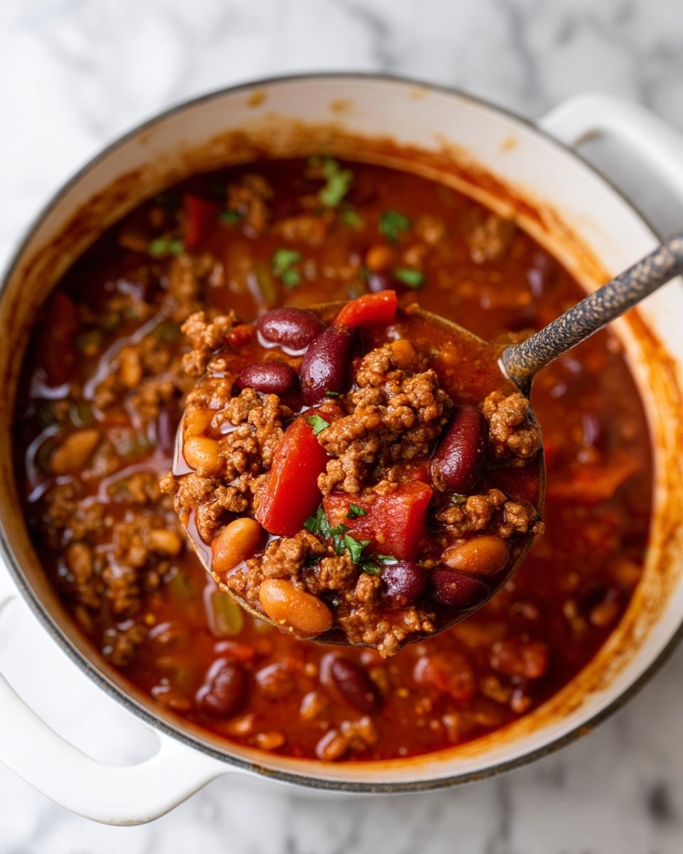 The dish shows a thick chili stew in a white bowl with a yellow rim, filled mainly with cooked ground meat and kidney beans mixed with diced tomatoes and small green bell pepper pieces, all covered in a rich reddish-brown sauce. On top, there is a dollop of smooth white sour cream placed near a bright green lime wedge resting on the stew. To the side of the sour cream, there is a small pile of curled yellow tortilla chip pieces, some fresh green cilantro leaves, and a sprinkle of shredded cheese in white and orange colors. The bowl sits on a white marbled surface. Photo taken with an iphone --ar 4:5 --v 7