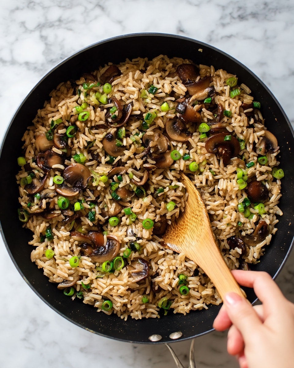 A close-up image of a bowl filled with cooked rice and sliced mushrooms mixed together. The rice is light brown with some green pieces of herbs or spring onions scattered on top, adding a fresh contrast. The mushroom slices are soft, brown, and slightly shiny, sitting evenly throughout the rice. The bowl is white, with a textured look around the edge, and a spoon with a silver handle is placed inside the bowl on the right side. The background is a white marbled surface, making the colors of the food stand out. Photo taken with an iphone --ar 4:5 --v 7